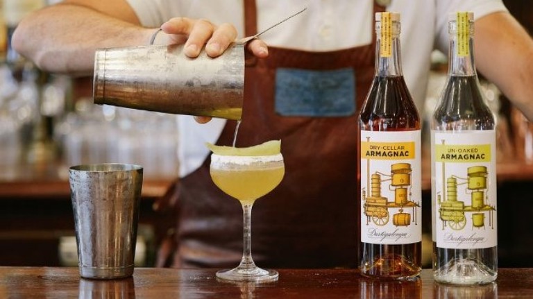 Two bottles of cognac and a cocktail being poured into a coupe