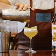 Two bottles of cognac and a cocktail being poured into a coupe