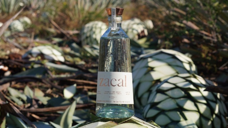 A bottle of Zacal Mezcal with harvested agave plants in the background